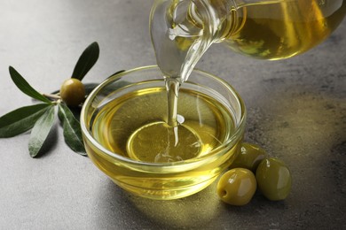 Pouring olive oil into glass bowl on grey table, closeup Photo of Pouring olive oil into glass bowl on grey table, closeup