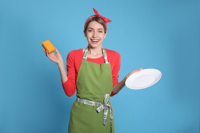 Young housewife with plate and sponge on light blue background Photo of Young housewife with plate and sponge on light blue background
