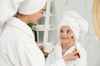 Young mother applying mask onto daughter's face in bathroom Photo of Young mother applying mask onto daughter's face in bathroom