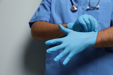 Photo of Doctor putting on medical gloves against light grey background, closeup