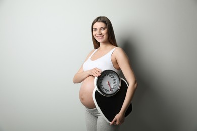 Pregnant woman with scales on grey background Photo of Pregnant woman with scales on grey background