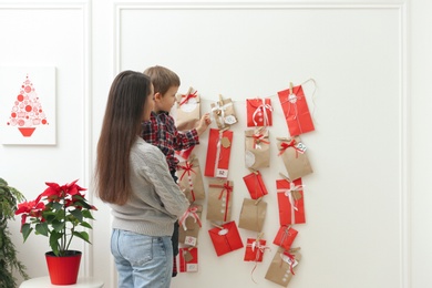 Mother and son taking gift from Advent calendar at home. Christmas tradition Photo of Mother and son taking gift from Advent calendar at home. Christmas tradition