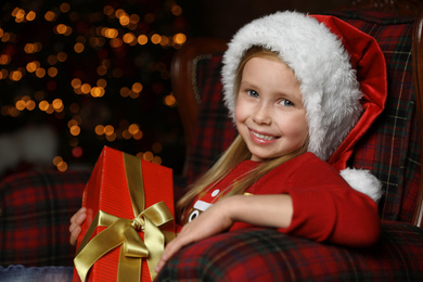 Cute little child with Christmas gift sitting in armchair at home Photo of Cute little child with Christmas gift sitting in armchair at home