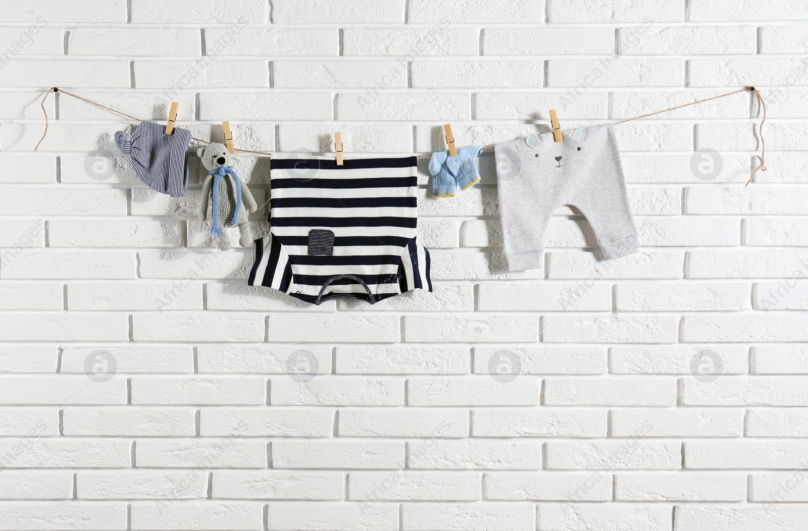 Baby clothes hanging on washing line near white brick wall Photo of Baby clothes hanging on washing line near white brick wall