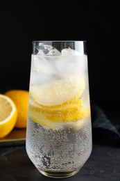 Soda water with lemon slices and ice cubes on black table Photo of Soda water with lemon slices and ice cubes on black table