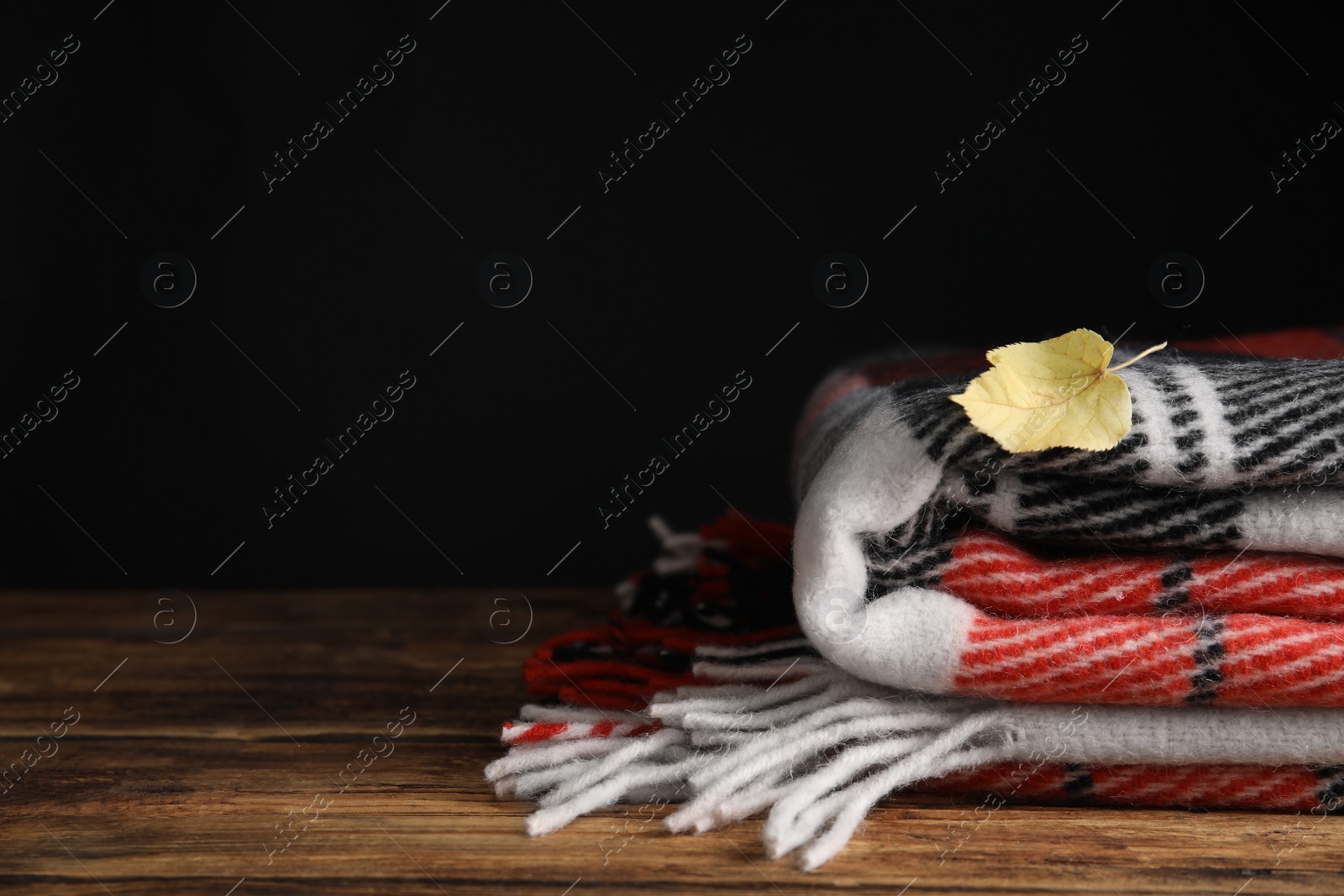 Checkered plaid and dry leaf on wooden table, closeup. Space for text Photo of Checkered plaid and dry leaf on wooden table, closeup. Space for text