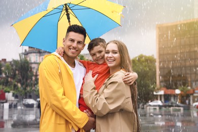 Happy family with umbrella walking under rain on city street Photo of Happy family with umbrella walking under rain on city street