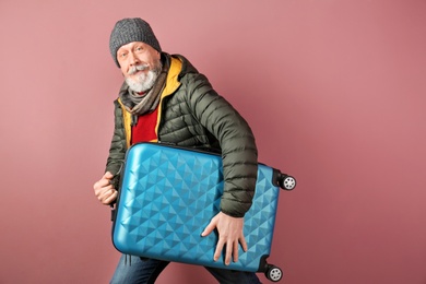 Mature man with suitcase on color background. Ready for winter vacation Photo of Mature man with suitcase on color background. Ready for winter vacation