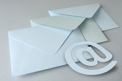 White paper envelopes and at sign on light grey background, closeup. Email service Image of White paper envelopes and at sign on light grey background, closeup. Email service