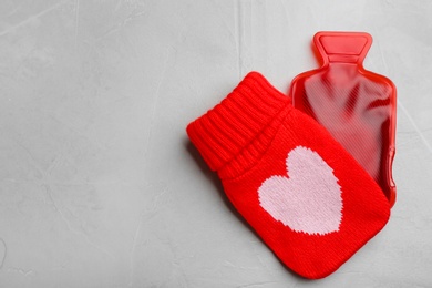 Photo of Hot water bottle with knitted cover on grey stone background, flat lay. Space for text