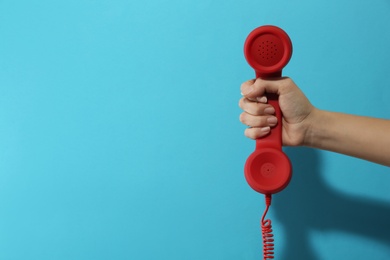 Closeup view of woman holding red corded telephone handset on light blue background, space for text. Hotline concept Photo of Closeup view of woman holding red corded telephone handset on light blue background, space for text. Hotline concept