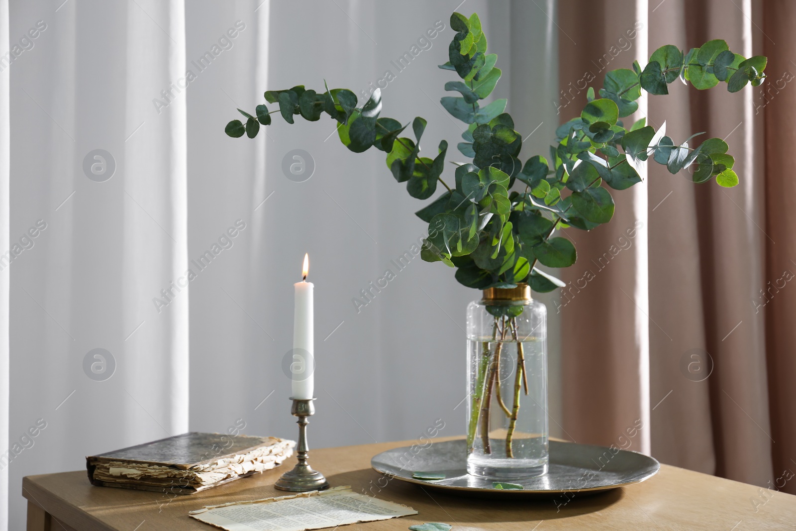 Beautiful eucalyptus branches, old book and holder with burning candle on wooden table indoors. Interior element Photo of Beautiful eucalyptus branches, old book and holder with burning candle on wooden table indoors. Interior element