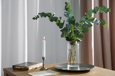 Beautiful eucalyptus branches, old book and holder with burning candle on wooden table indoors. Interior element Photo of Beautiful eucalyptus branches, old book and holder with burning candle on wooden table indoors. Interior element
