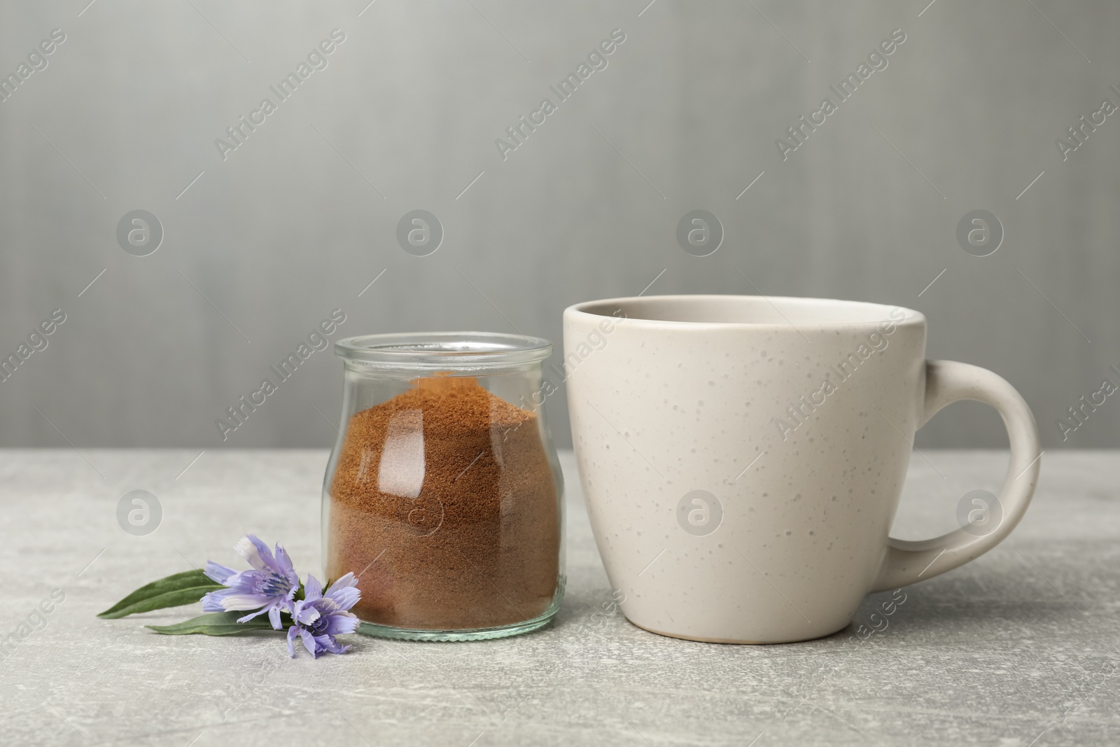 Jar with chicory powder, cup and flowers on light grey table Photo of Jar with chicory powder, cup and flowers on light grey table