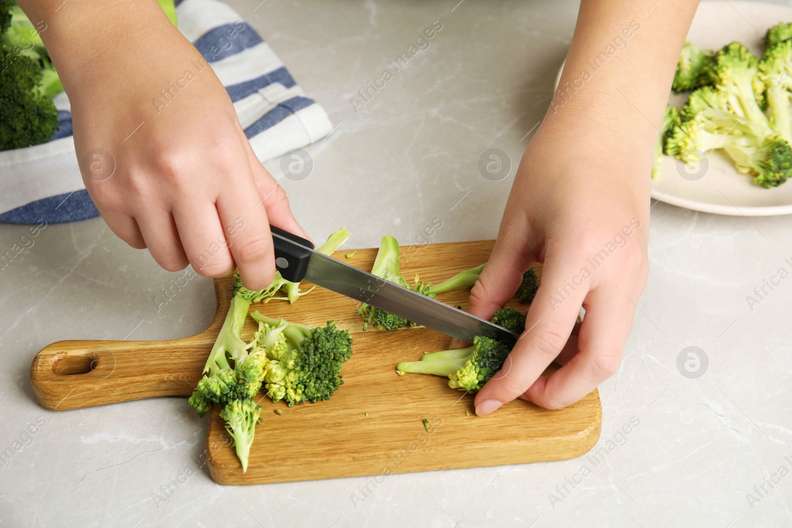 Woman cutting raw broccoli at light grey marble table, closeup Photo of Woman cutting raw broccoli at light grey marble table, closeup