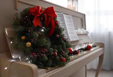 White piano with decorative wreath indoors, closeup. Christmas music Photo of White piano with decorative wreath indoors, closeup. Christmas music