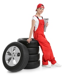 Female mechanic in uniform with car tires and clipboard on white background Photo of Female mechanic in uniform with car tires and clipboard on white background