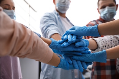 Group of people in blue medical gloves stacking hands indoors, closeup Photo of Group of people in blue medical gloves stacking hands indoors, closeup