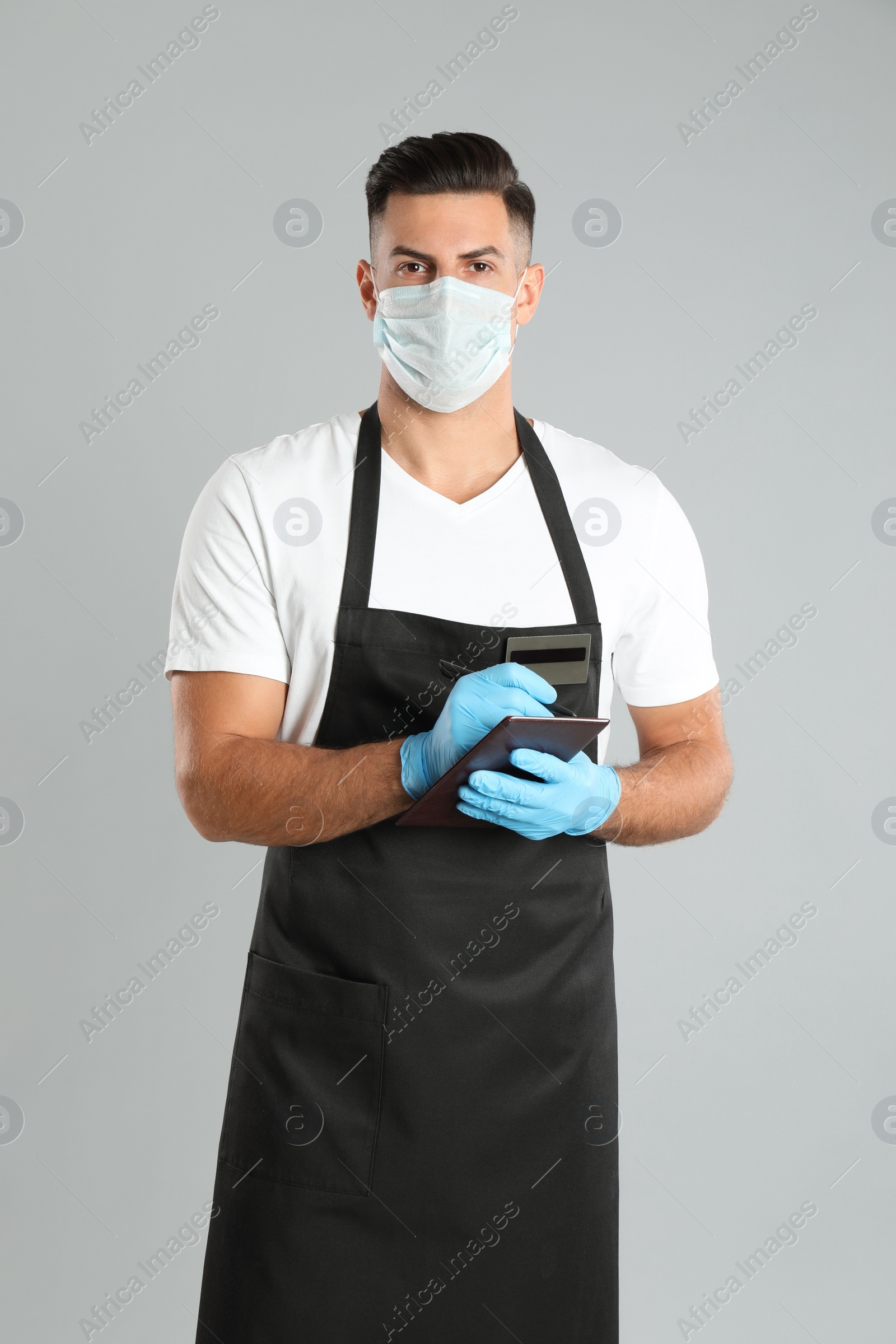 Waiter in medical face mask taking order on light grey background Photo of Waiter in medical face mask taking order on light grey background