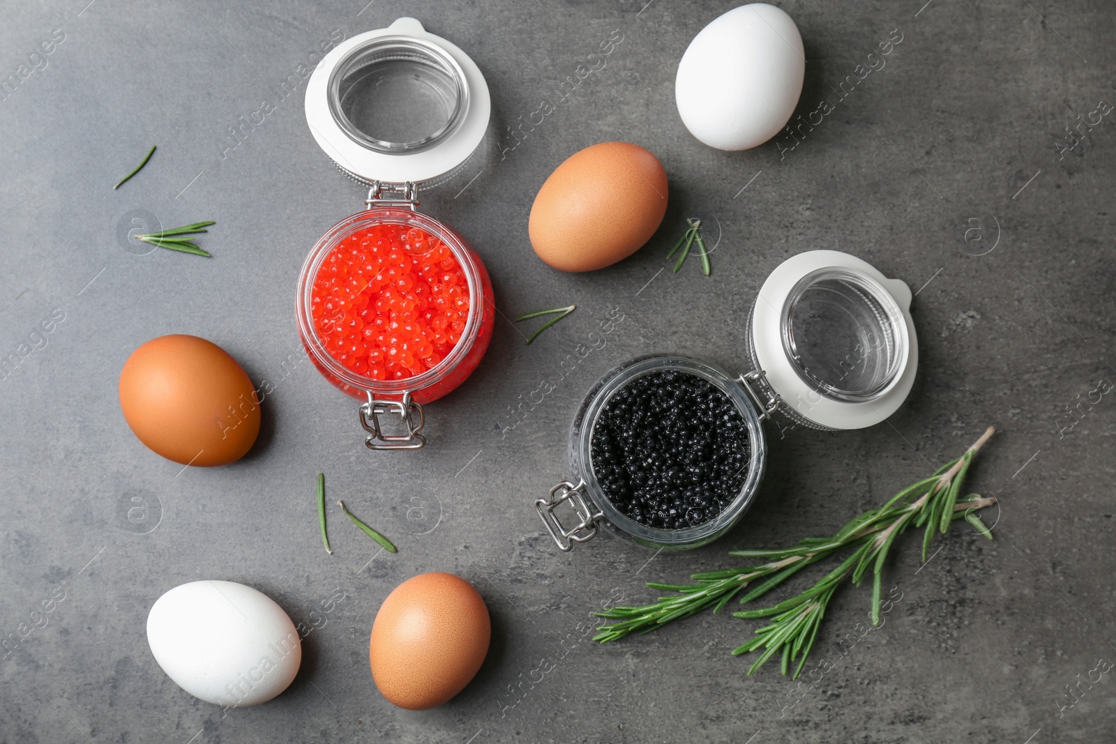 Glass jars with black and red caviar on grey background Photo of Glass jars with black and red caviar on grey background