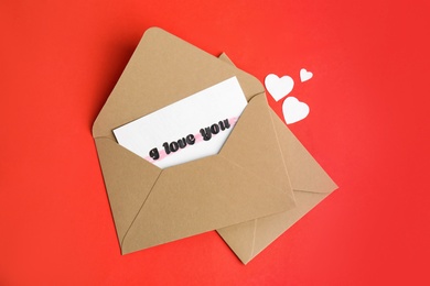 Card with phrase I Love You in envelope and paper hearts on red background, flat lay Photo of Card with phrase I Love You in envelope and paper hearts on red background, flat lay