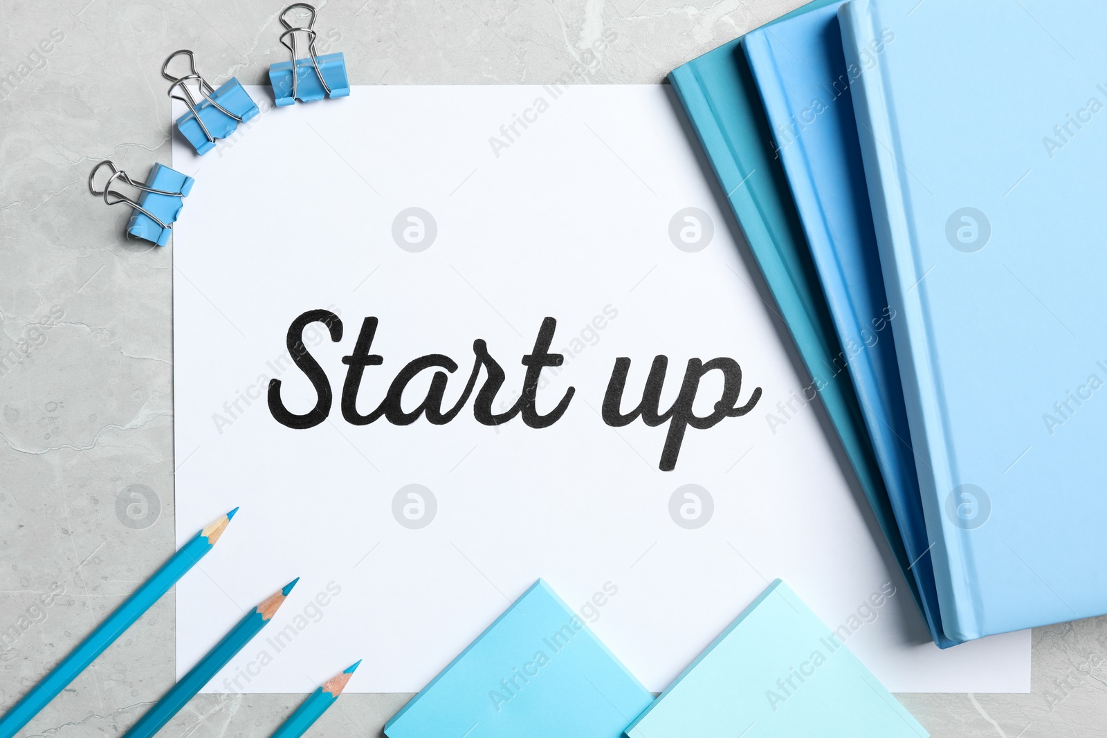Sheet of paper with phrase Start Up and stationery on grey table, flat lay Photo of Sheet of paper with phrase Start Up and stationery on grey table, flat lay