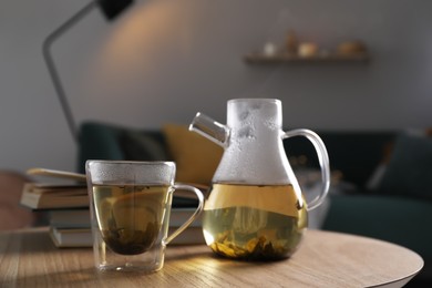 Glass teapot and cup of hot tea on wooden table in living room. Cozy home atmosphere Photo of Glass teapot and cup of hot tea on wooden table in living room. Cozy home atmosphere