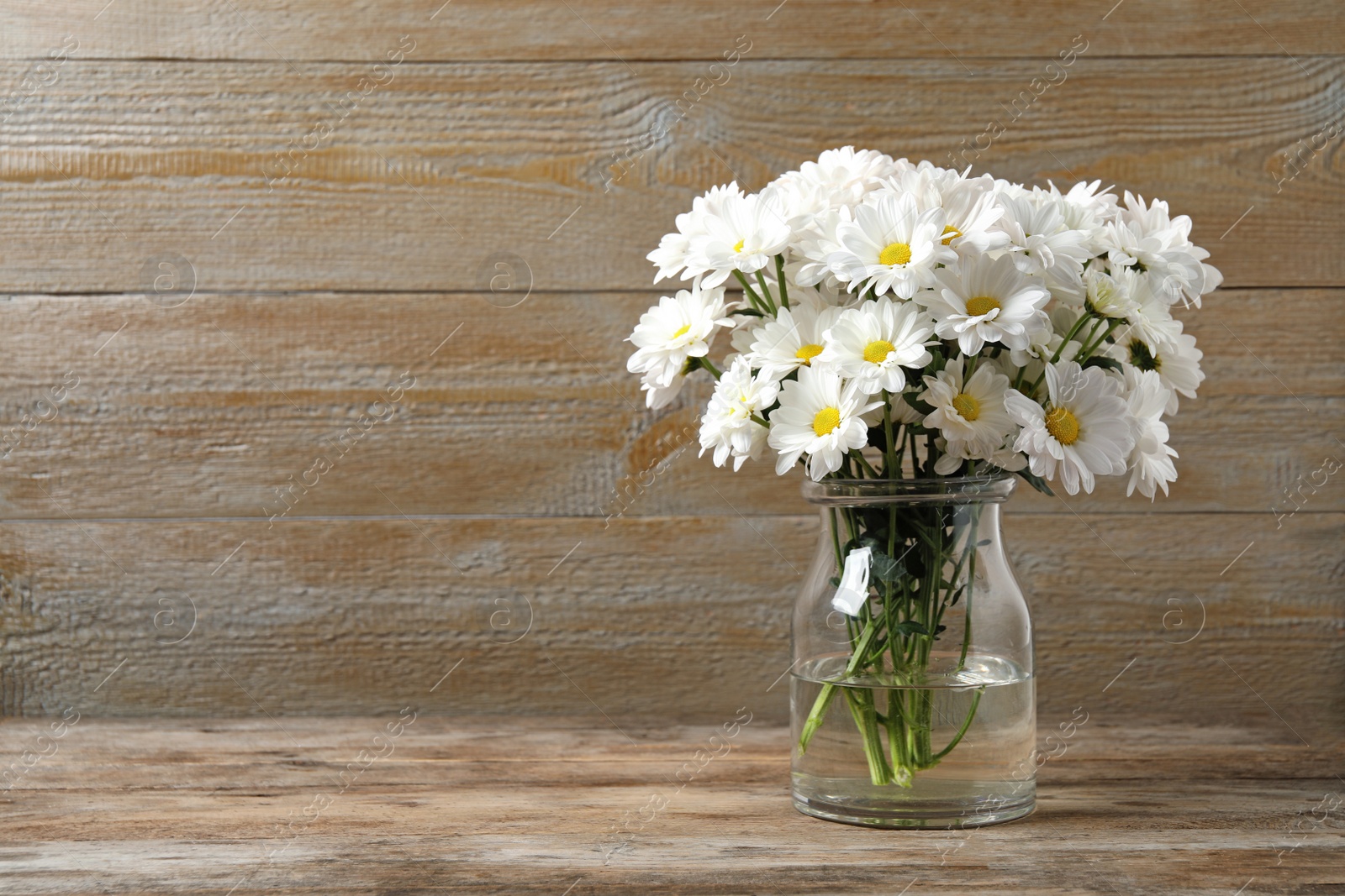 Beautiful white chrysanthemum flowers in glass vase on table. Space for text Photo of Beautiful white chrysanthemum flowers in glass vase on table. Space for text
