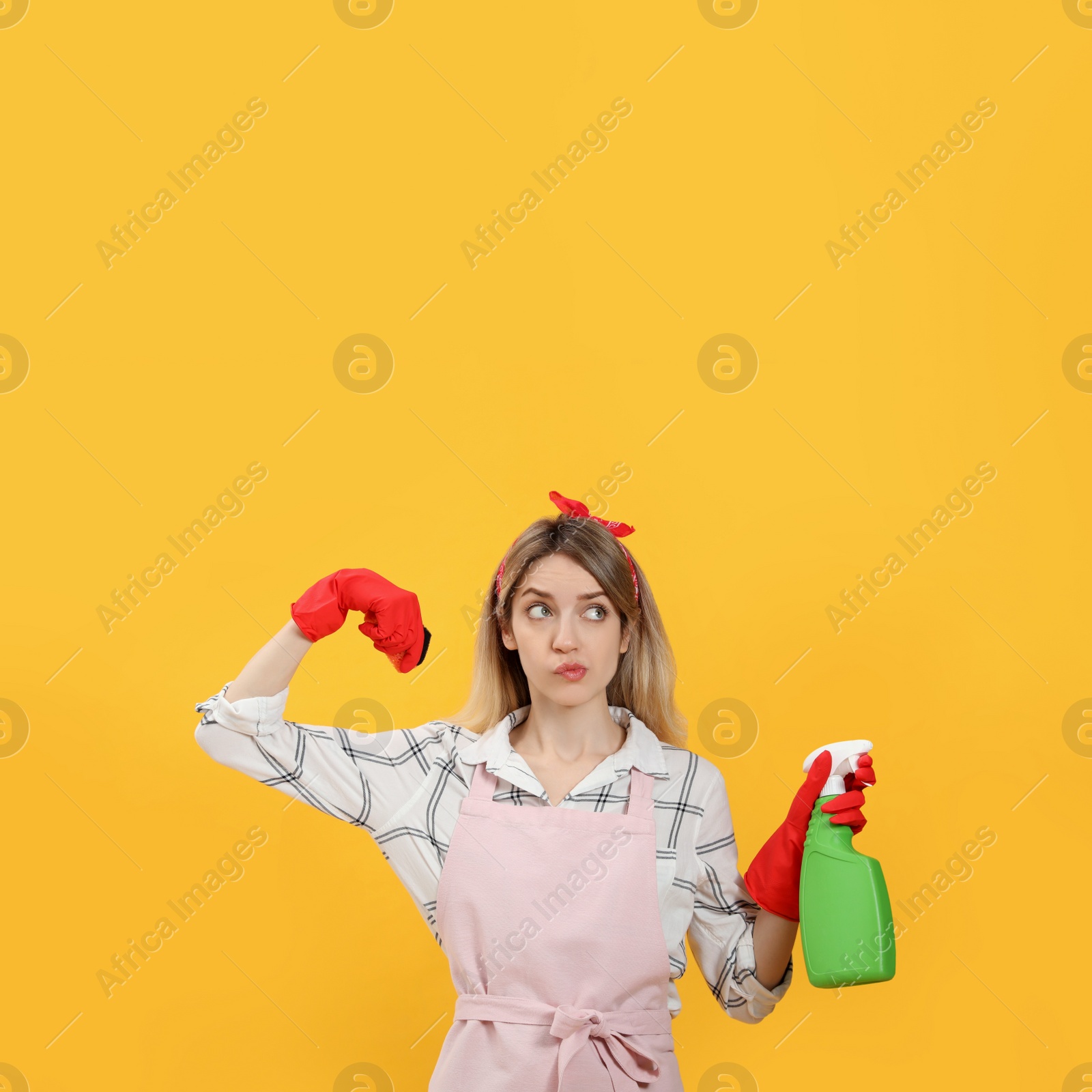 Young housewife with detergent and sponge on yellow background Photo of Young housewife with detergent and sponge on yellow background