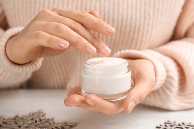 Woman holding jar of cream at light table, closeup. Cosmetic product for winter Photo of Woman holding jar of cream at light table, closeup. Cosmetic product for winter