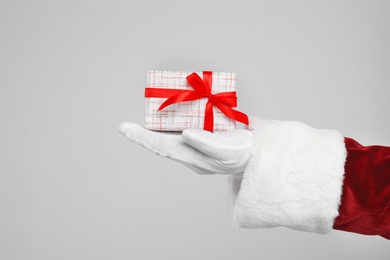 Santa Claus holding Christmas gift on light grey background, closeup of hand Photo of Santa Claus holding Christmas gift on light grey background, closeup of hand