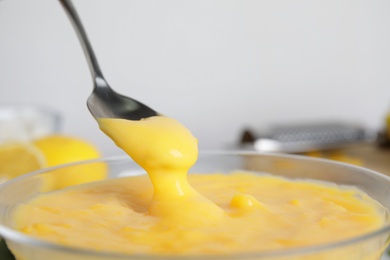 Photo of Spoon with delicious lemon curd above bowl, closeup