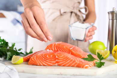 Woman salting fresh raw salmon at table, closeup. Fish delicacy Photo of Woman salting fresh raw salmon at table, closeup. Fish delicacy