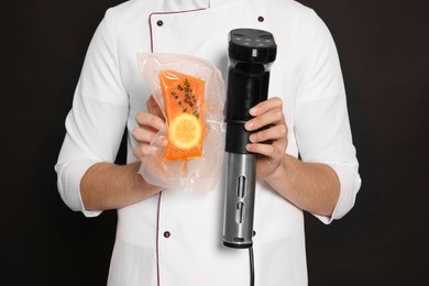 Photo of Chef holding sous vide cooker and salmon in vacuum pack on black background, closeup