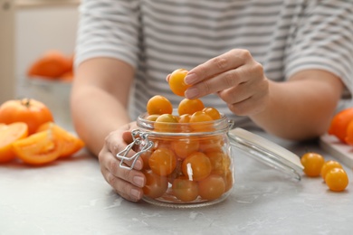 Woman putting yellow tomatoes into glass jar at light kitchen table, closeup. Pickling vegetables Photo of Woman putting yellow tomatoes into glass jar at light kitchen table, closeup. Pickling vegetables