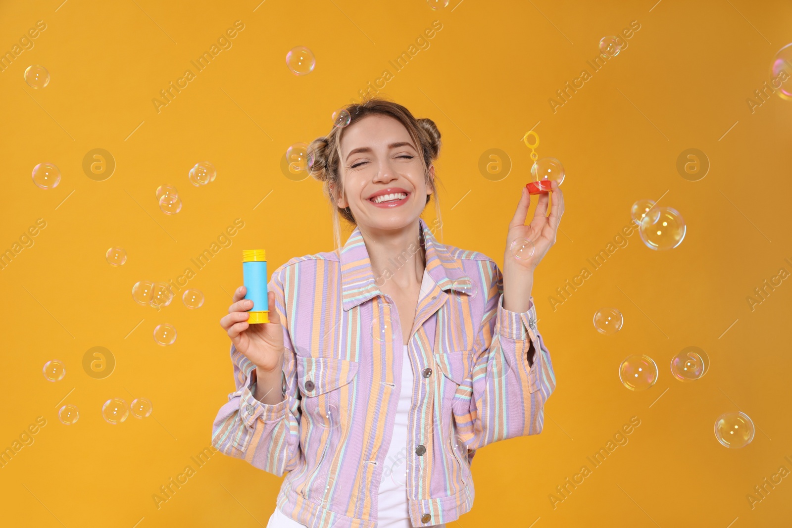 Young woman blowing soap bubbles on yellow background Photo of Young woman blowing soap bubbles on yellow background