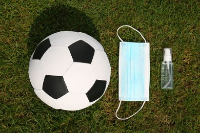 Football ball with hand sanitizer and protective mask on green grass, flat lay Photo of Football ball with hand sanitizer and protective mask on green grass, flat lay