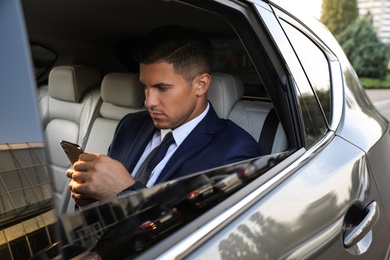 Handsome man with smartphone on backseat of modern car Photo of Handsome man with smartphone on backseat of modern car