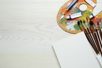 Blank canvas, tools, palette and paints on white wooden table, flat lay. Space for text Photo of Blank canvas, tools, palette and paints on white wooden table, flat lay. Space for text