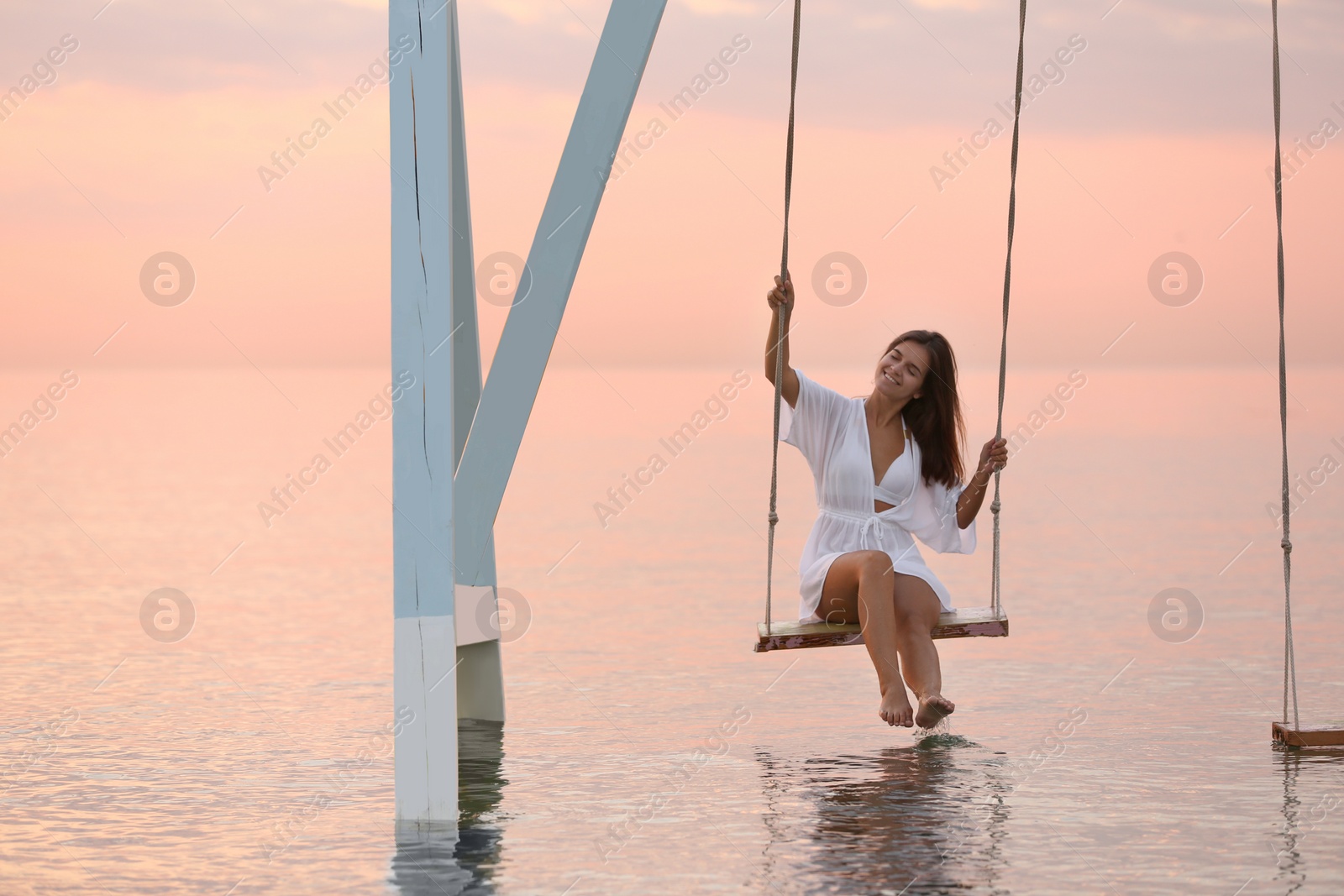 Young woman enjoying sunrise on swing over water Photo of Young woman enjoying sunrise on swing over water