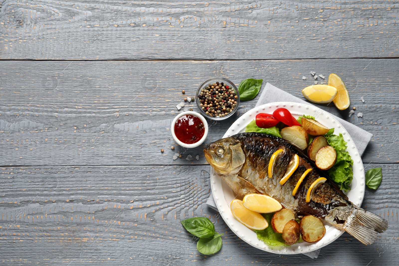 Photo of Tasty homemade roasted crucian carp served on grey wooden table, flat lay and space for text. River fish