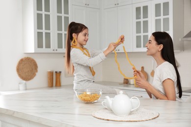 Young mother and her daughter with necklaces made of pasta having fun in kitchen Photo of Young mother and her daughter with necklaces made of pasta having fun in kitchen