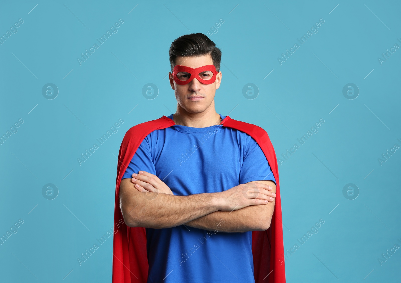 Man wearing superhero cape and mask on light blue background Photo of Man wearing superhero cape and mask on light blue background