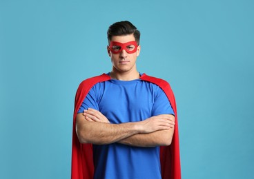 Man wearing superhero cape and mask on light blue background Photo of Man wearing superhero cape and mask on light blue background