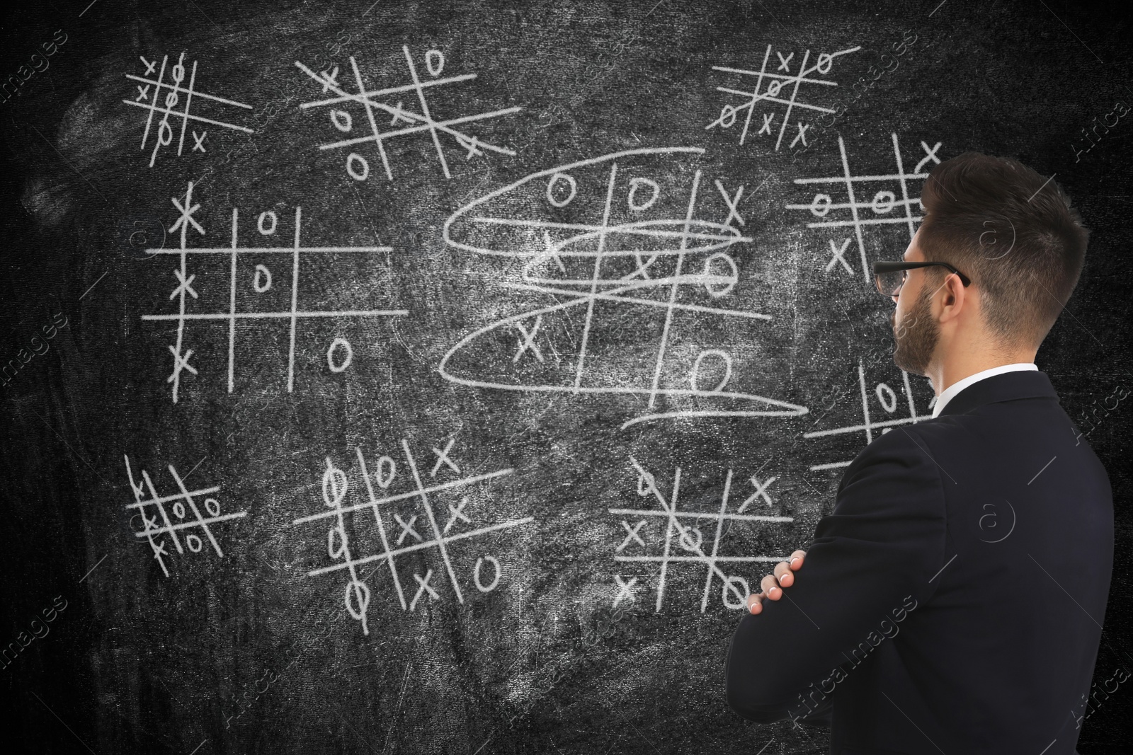 Young businessman in elegant suit near blackboard with drawn tic tac toe game Image of Young businessman in elegant suit near blackboard with drawn tic tac toe game