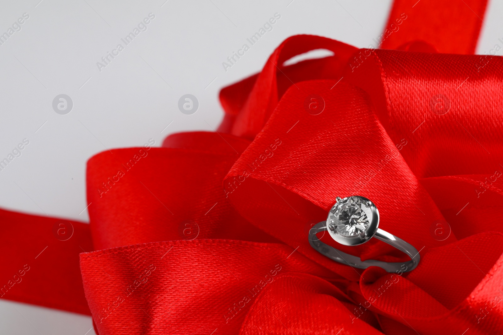 Beautiful red bow and engagement ring on white background, closeup Photo of Beautiful red bow and engagement ring on white background, closeup
