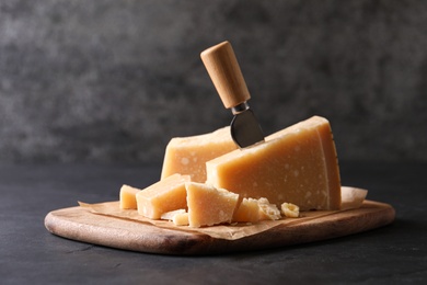 Delicious parmesan cheese with knife on black table Photo of Delicious parmesan cheese with knife on black table