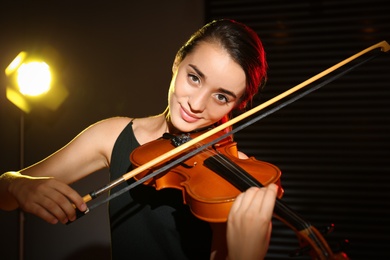 Beautiful young woman playing violin in dark room Photo of Beautiful young woman playing violin in dark room