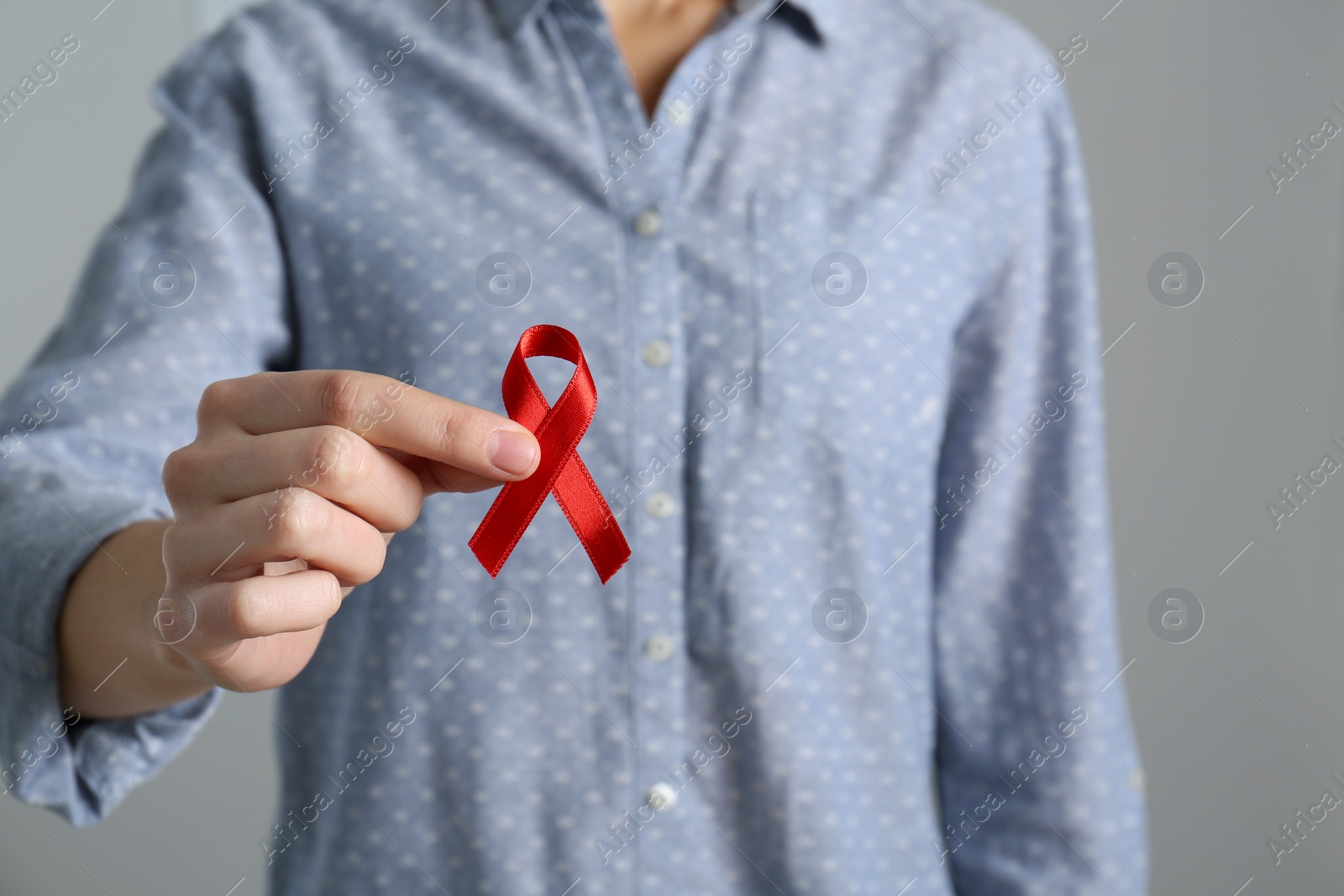 Woman holding red awareness ribbon on grey background, closeup with space for text. World AIDS disease day Photo of Woman holding red awareness ribbon on grey background, closeup with space for text. World AIDS disease day