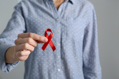 Woman holding red awareness ribbon on grey background, closeup with space for text. World AIDS disease day Photo of Woman holding red awareness ribbon on grey background, closeup with space for text. World AIDS disease day